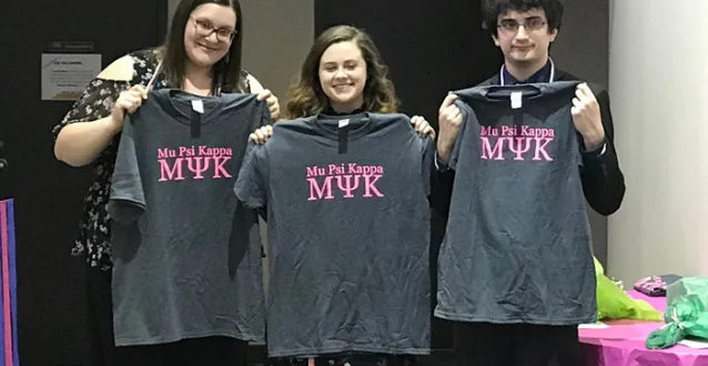 Three students holding up Mu Psi Kappa T-shirts