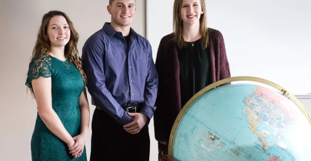 3 Marietta students standing behind a large globe