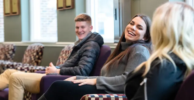 Female student smiling in between a male student on left and blonde female on right