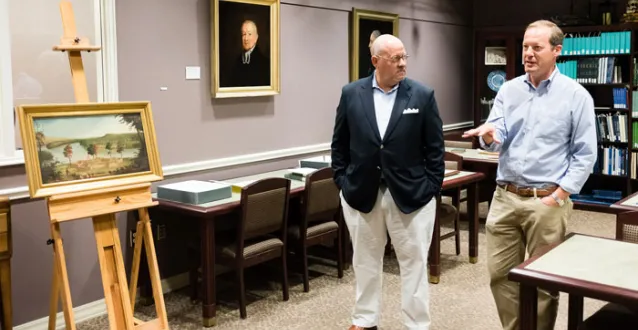 Two men in the library talking about an old painting