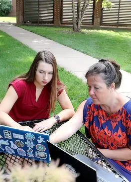 Professor Suzanne Parsons and a Biochemistry student looking at a laptop while sitting at a picnic table outdoors.