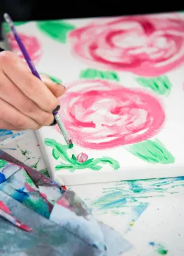 A hand holding a paint brush and painting flowers