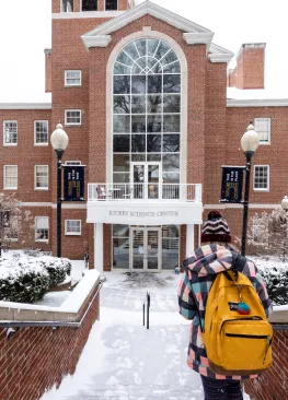 A student walks down the snow covered stairs in front of Rickey Science Center
