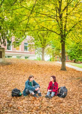 Students sitting on a leaf covered lawn during fall at Marietta College