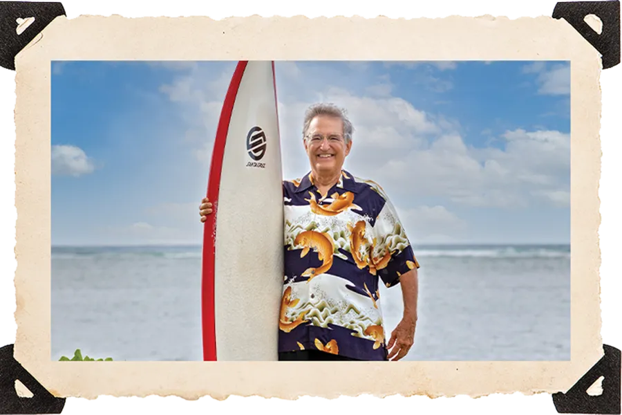 Kenneth Andrus poses with a surf board on the beach